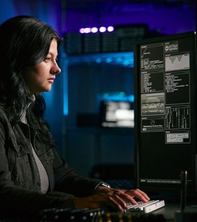Low Key Lighting Shot Of Female Computer Hacker Sitting In Front Low Key Lighting Shot Of Female Computer Hacker Sitting In Front Of Screens Breaching Cyber Security