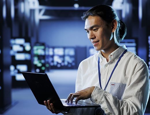 Worker prevents server system overload Qualified engineer in data center using laptop to prevent system overload during peak traffic periods. Diligent worker in server room ensuring there is enough network bandwidth for smooth operations